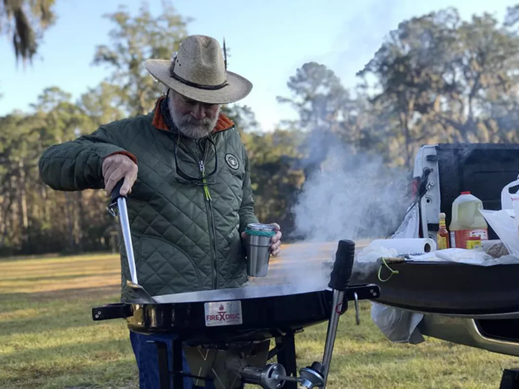 Man using his FIREDISC to cook in nature off the back of his truck.