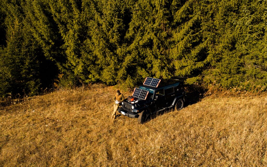 Outdoorsman leaning against his Jeep as his portable solar power station.  Looks and feels at ease