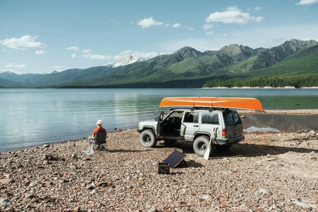 A guy fishes by a lake with solar power charging behind him